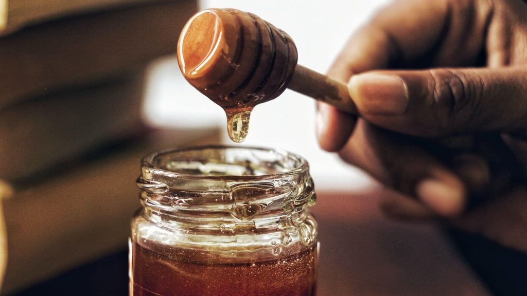A glass jar filled with golden, natural honey, glistening in the light, perfect for some homemade skincare.